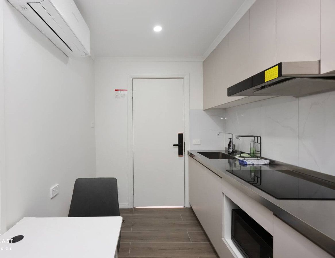 A compact kitchen with a white countertop, a black chair, and a door leading to another room.