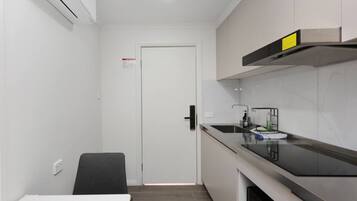 A compact kitchen with a white countertop, a black chair, and a door leading to another room.