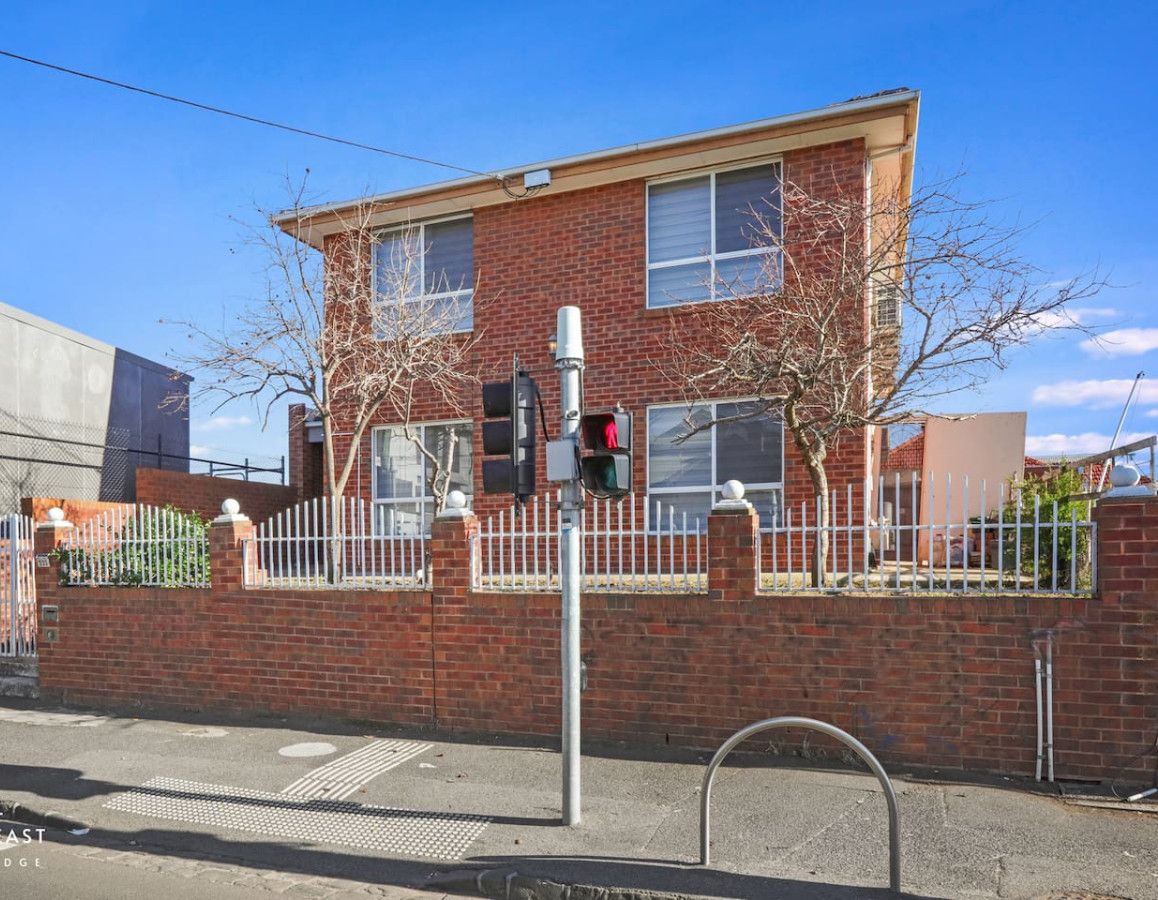 A two-story brick building with a white fence, a traffic light, and a pedestrian crossing.