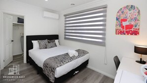 Ein Schlafzimmer mit Bett, Schreibtisch, Stuhl, Fenster mit Jalousien und einem Wandbild.