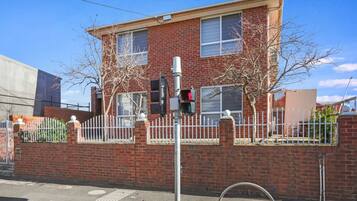 A two-story brick house with a white fence, a traffic light, and a pedestrian crossing.