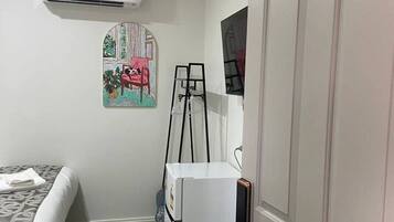 A room with a bed, a white refrigerator, a black trash bin, a painting on the wall, and a door with the number 106.
