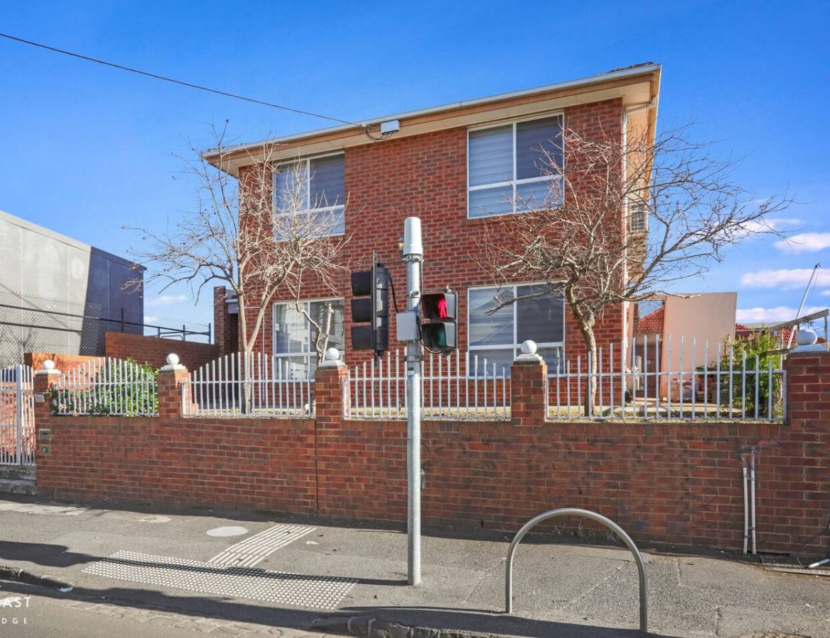 A two-story brick house with a white fence, a traffic light, and a pedestrian crossing.