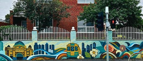 A two-story brick house with a white fence and colorful mural.