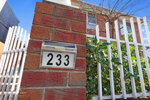Una pared de ladrillo con una placa de número de casa '233' y una cerca blanca de piquetes.