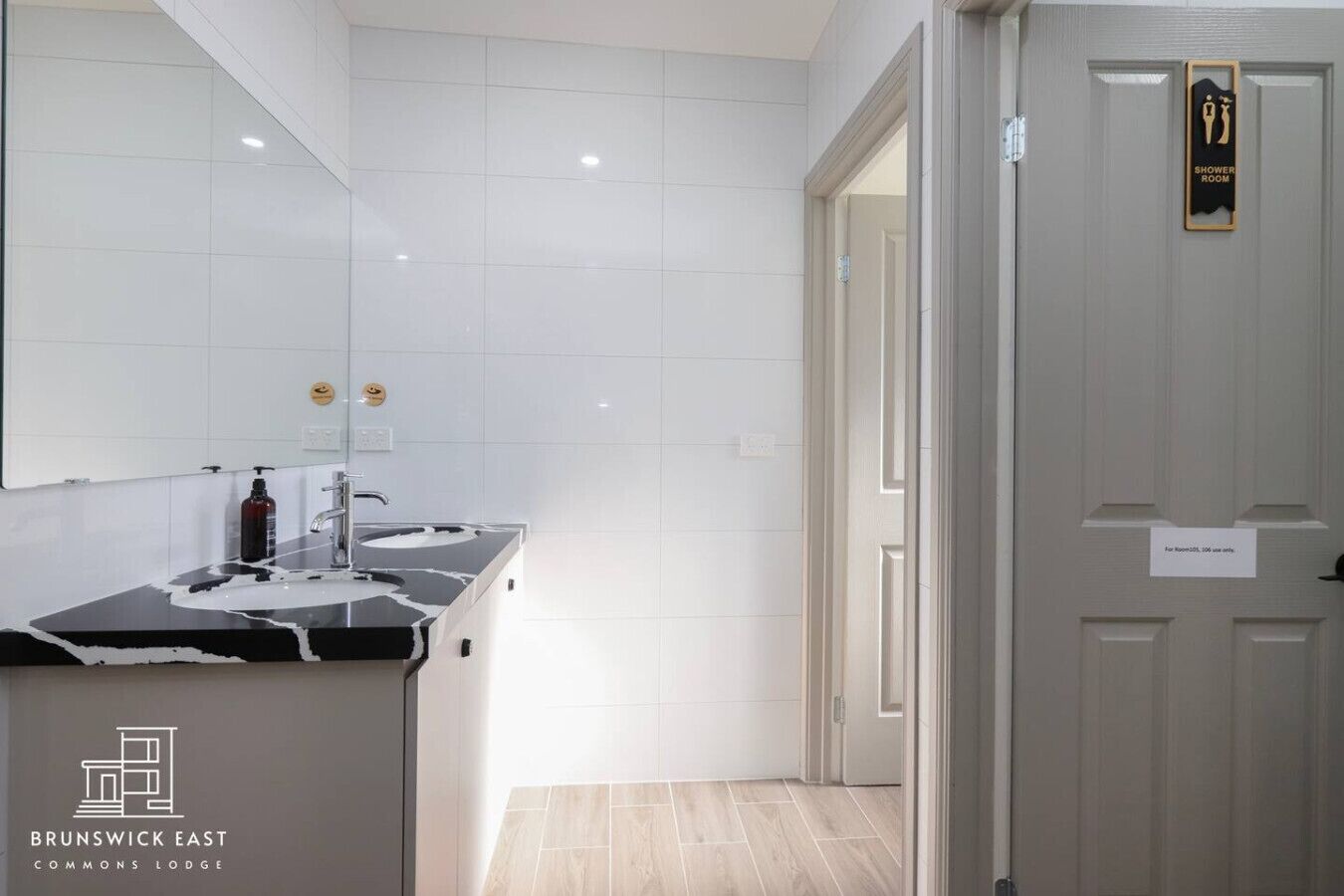 A bathroom with a black countertop sink, white tiles, and a shower sign on the door.