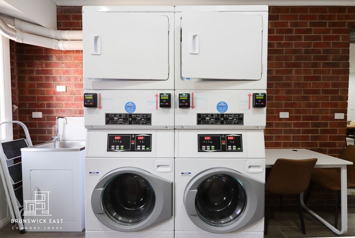 A laundry area with four washing machines and two dryers, a sink, and a table with chairs.