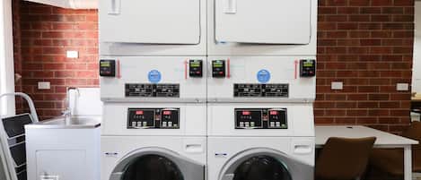 A laundry area with four washing machines and two dryers, a sink, and a table with chairs.