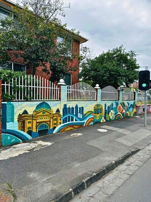 A street with a colorful mural on the wall, a white fence, and a traffic light.
