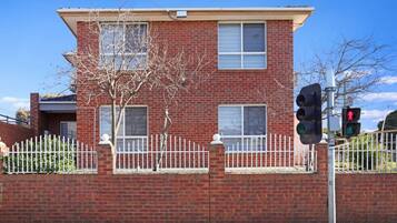 A two-story brick building with a white picket fence, a tree in front, and a traffic light.