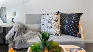 A modern living room with a grey sofa, patterned cushions, a fluffy grey throw, and a small potted plant on a coffee table.