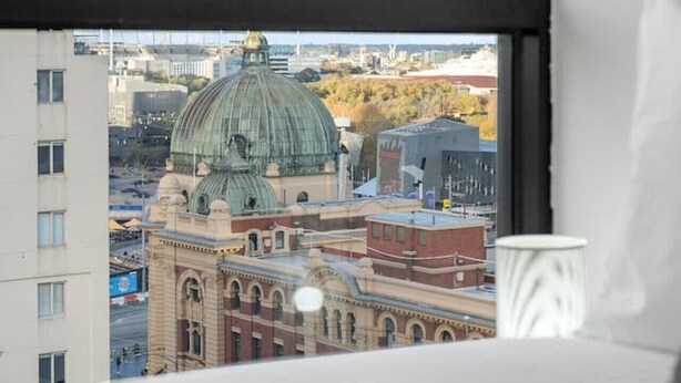 A hotel room with a large window offering a view of a cityscape, including a prominent green-domed building.