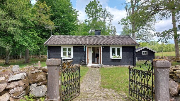 A rustic cabin with a stone wall entrance, a wooden door, and a small porch.