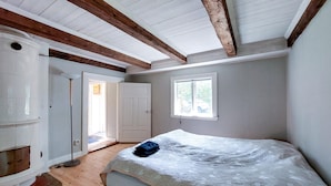 A bedroom with a wooden floor, a bed with a white mattress, a window with a view of the outside, and a door leading to another room.
