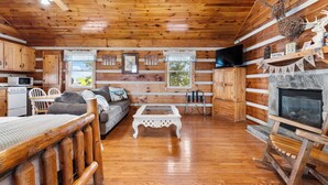 A log cabin interior with a wooden floor, a sofa, a coffee table, a fireplace, a television, and a dining area with a table and chairs. - Hillside Hideout Log Cabin For 2!  Cabin 10 (Fancy Gap)
