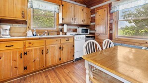 A wooden cabin-style kitchen with wooden cabinets, a wooden table, and a white stove. - Hillside Hideout Log Cabin For 2!  Cabin 10 (Fancy Gap)