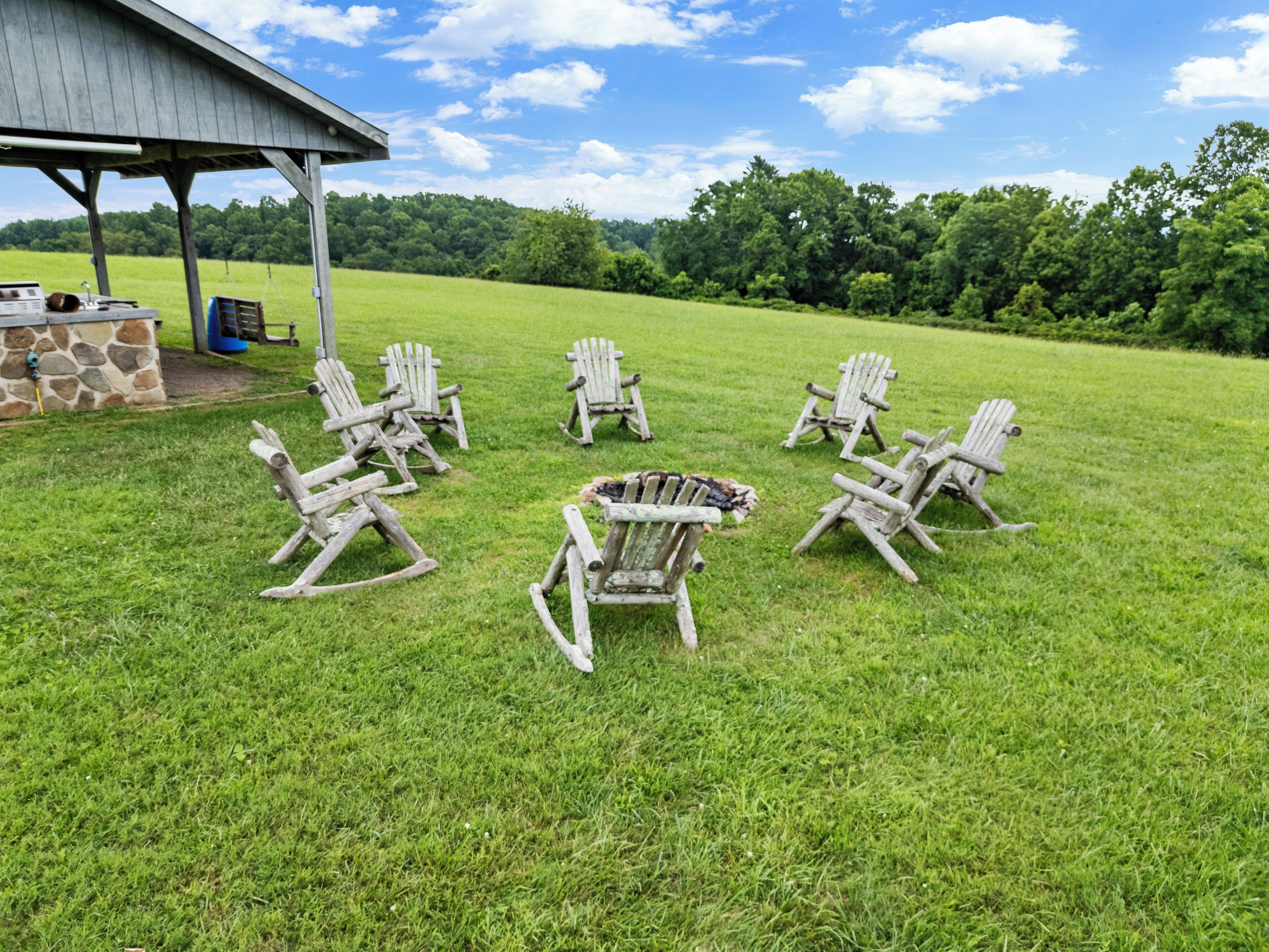 A grassy outdoor area with several Adirondack chairs arranged in a circle.