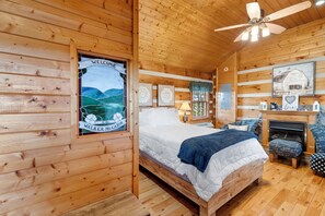 A wooden cabin room with a bed, a desk, a chair, and a fireplace. - Peaceful Pines Mountain Cabin with Jacuzzi and Views!  Cabin 12 (Fancy Gap)