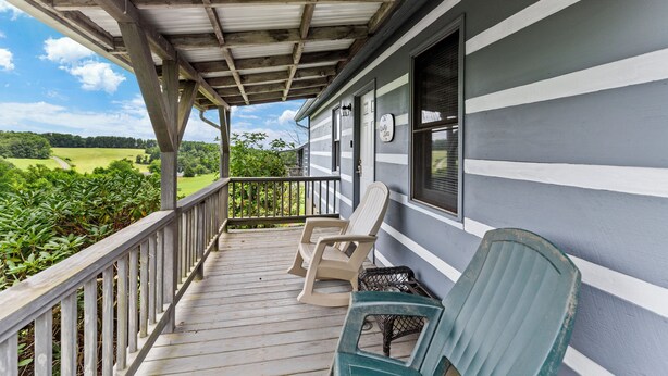 A covered porch with wooden railings, two rocking chairs, and a view of a green landscape.
