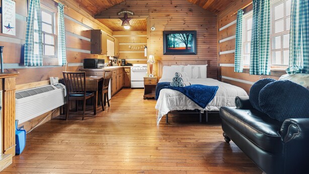 A cozy cabin-style room with a bed, a sofa, a dining area, and a kitchen.