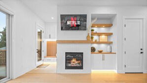 Ein modernes Wohnzimmer mit Kamin, einem Wand-Fernseher mit Netflix-Logo und einem Holzbodenregal mit Dekoration.