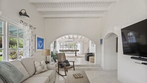 Un salon spacieux comprenant un canapé, un fauteuil et une table basse, une télévision, et donnant sur une piscine et un espace extérieur.