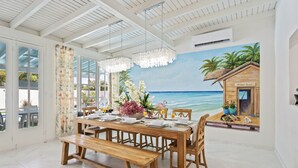 Un coin repas avec une table en bois dressée pour quatre personnes, un banc et une fresque murale représentant une scène de plage.