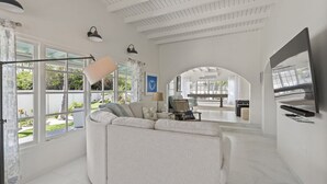 Un salon spacieux avec un grand canapé d’angle, un téléviseur à écran plat fixé au mur et une table de billard à l’arrière-plan.