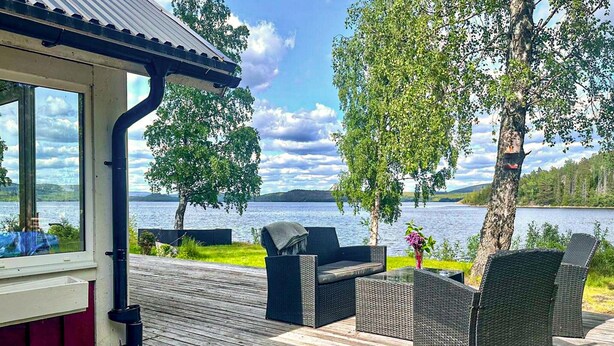A wooden deck with outdoor furniture, a covered area with windows, and a view of a lake and hills.