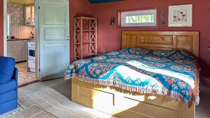 A bedroom with a bed, a wooden headboard, a window, and a door leading to a kitchen.