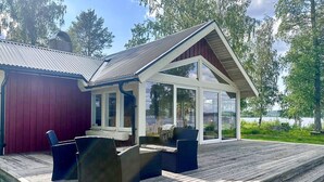 A wooden deck with outdoor furniture, a glass-enclosed porch, and a view of a lake.