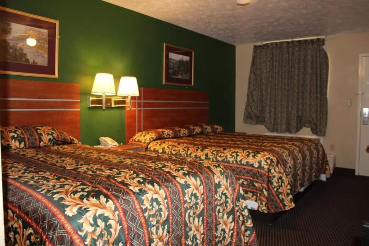 A hotel room with two beds, a telephone, wall-mounted lamps, and framed pictures.