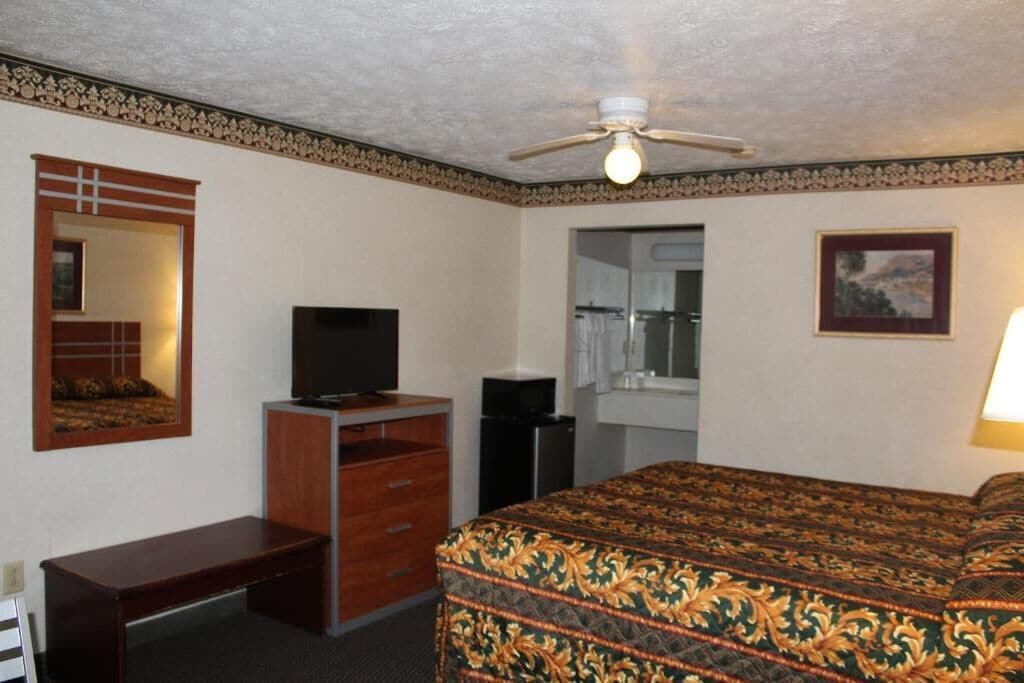 Ein Hotelzimmer mit Bett, Schreibtisch, Fernseher, Spiegel und Deckenventilator.