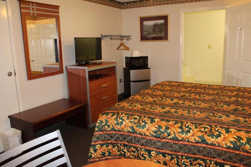 A hotel room with a bed, a desk with a television, a microwave, and a dresser.
