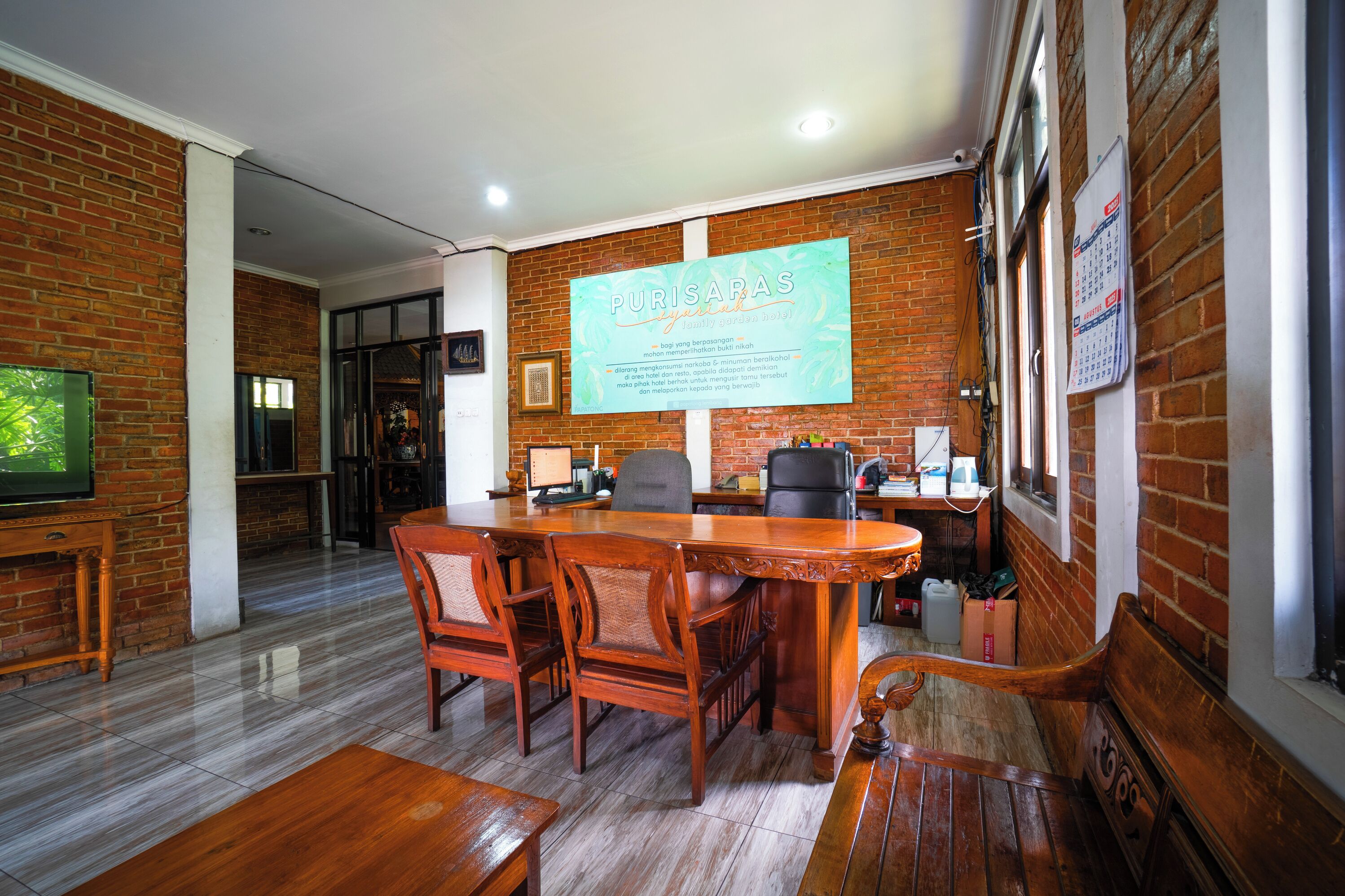 A conference room with a large wooden table, several chairs, a TV, and a brick wall with a calendar.