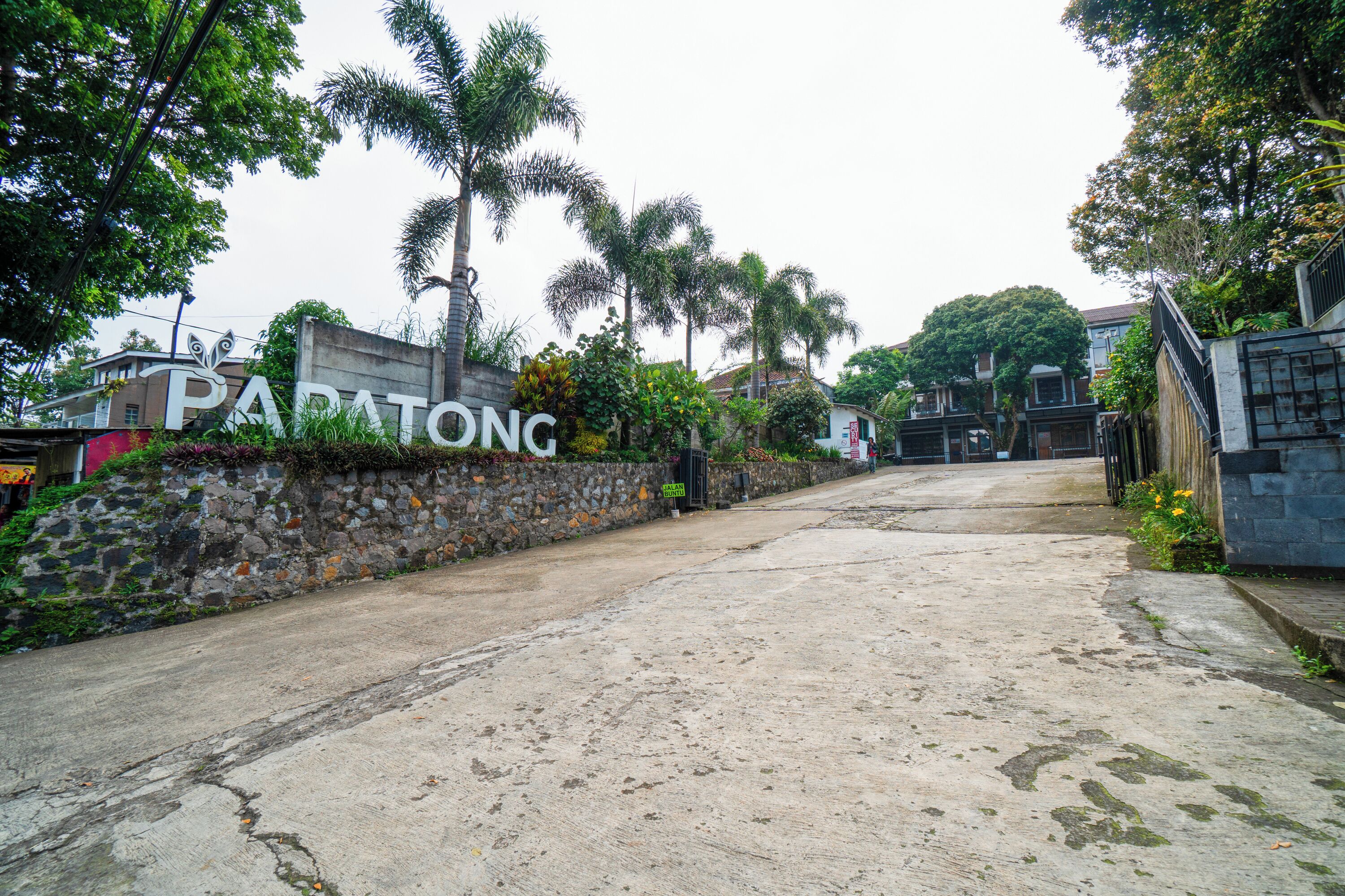 A paved entrance to a residential area with a stone wall and a sign reading "PARATONG".