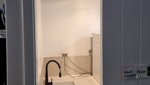 Une salle de bain avec un lavabo blanc, un robinet noir et un panneau indiquant qu’il s’agit d’une salle de toilette et de buanderie.