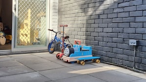 Un mur de briques avec une planche de bois au-dessus d’une porte de garage, un train jouet bleu et un vélo.