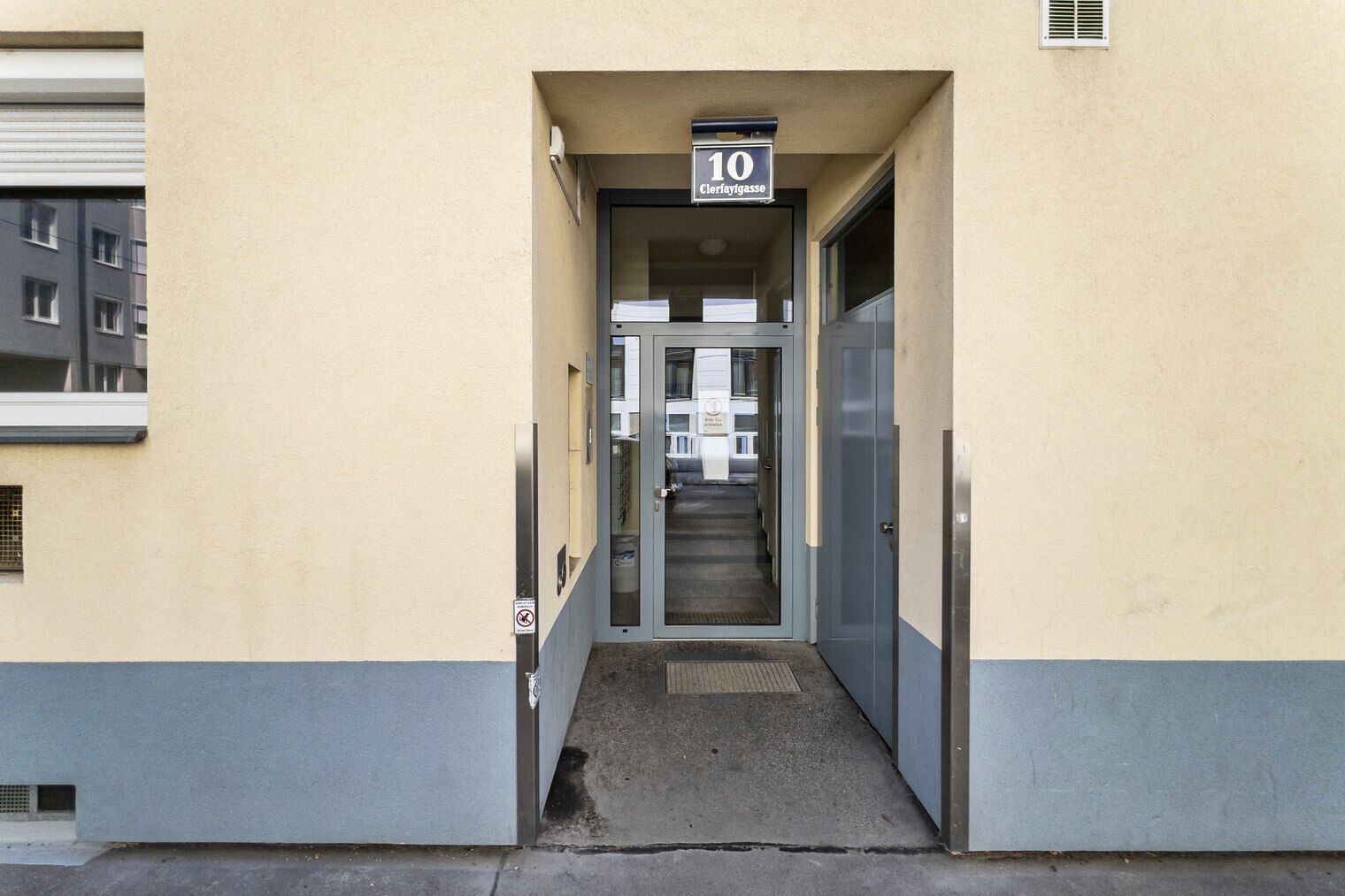 Entrada de um edifício com uma placa numérica '10' acima da porta, uma escadaria que leva para dentro e uma pequena janela à esquerda.