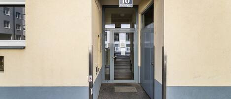 Entrada de um edifício com uma placa numérica '10' acima da porta, uma escadaria que leva para dentro e uma pequena janela à esquerda.