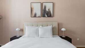A neatly made bed with two white pillows and a light-colored headboard. There are two bedside tables with lamps on either side of the bed.