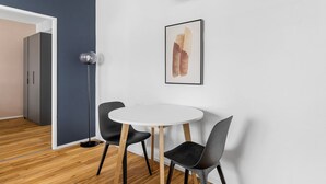 A modern room with a round white table, two black chairs, a floor lamp, and a framed abstract painting on the wall.