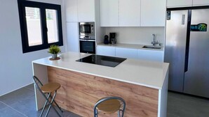 A modern kitchen with white cabinets, a built-in oven, a microwave, a stainless steel refrigerator, and a wooden island with two bar stools.