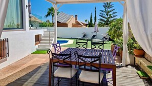 An outdoor patio with a wooden table and chairs, a pool, and a view of the surrounding neighborhood.