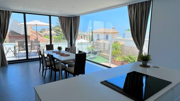 A modern kitchen with a large island, dining area with chairs, and a view of a pool and buildings.