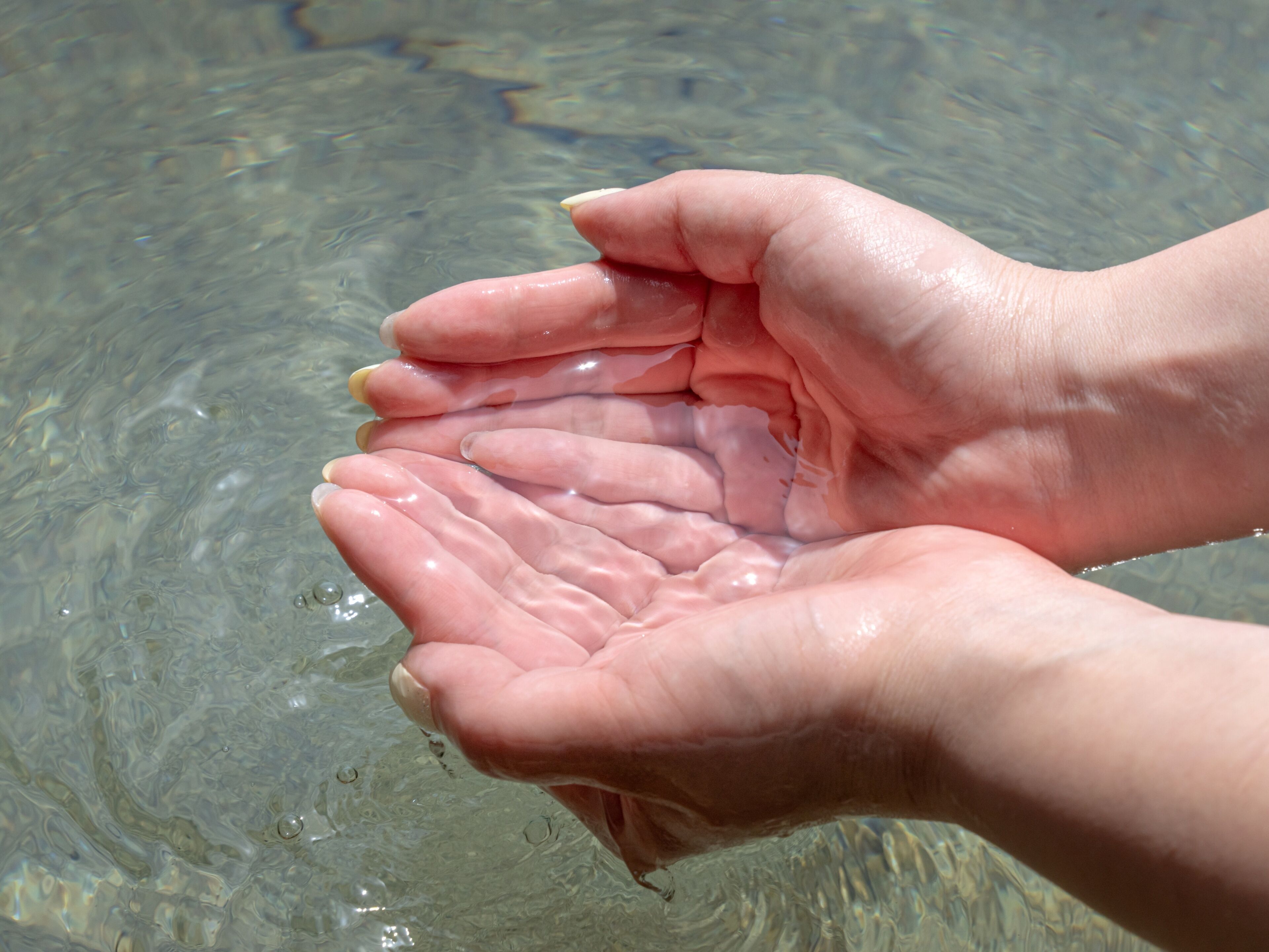 Hands cupped together over clear water, likely a pool or lake.