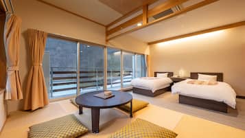 A modern hotel room with two beds, a round table, and large windows offering a view of the outdoors.