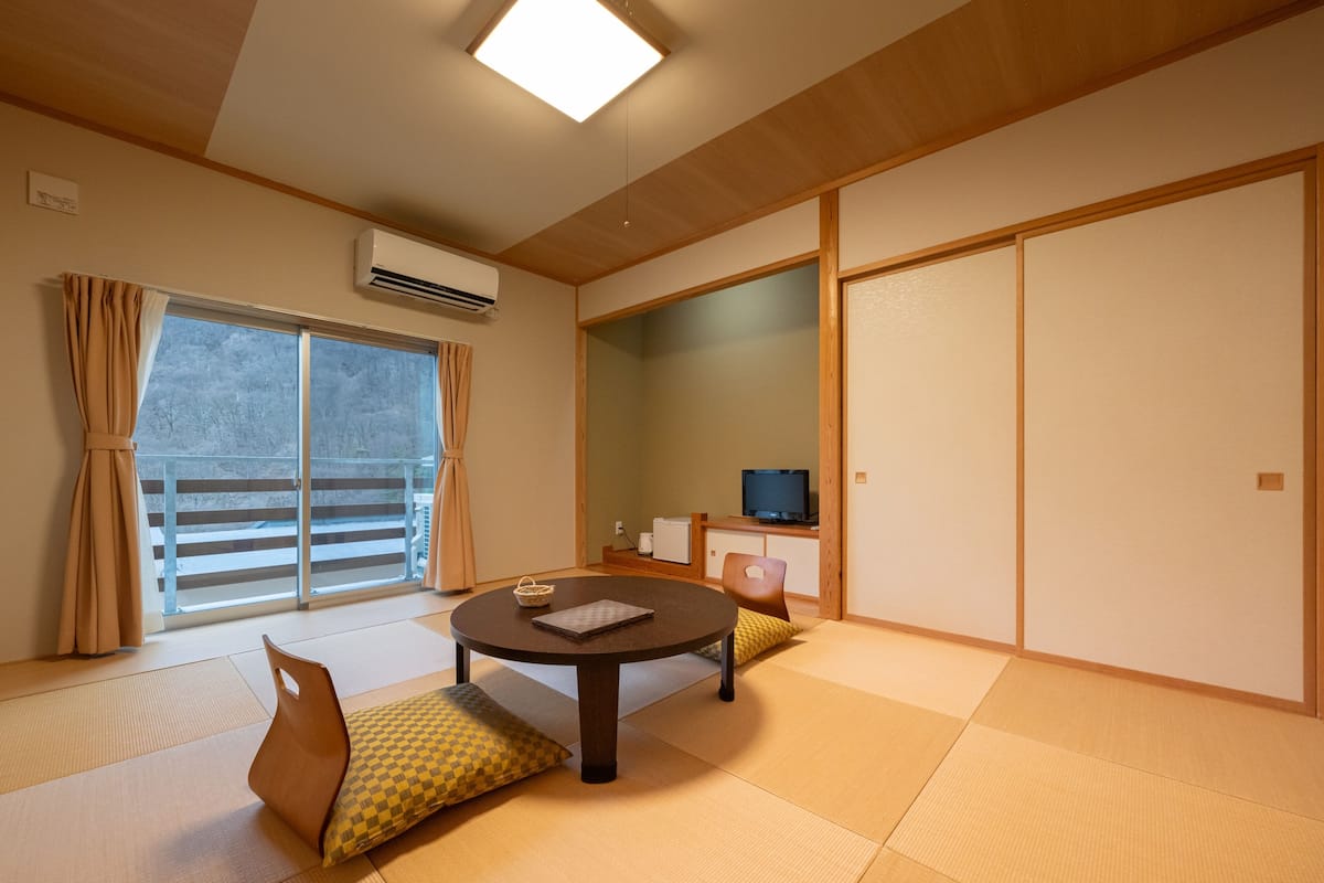 Una habitación japonesa tradicional con suelo de tatami, una mesa de tatami, un televisor y puertas correderas.