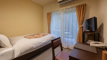 A hotel room with a bed, a desk, a chair, an air conditioner, a television, and a telephone.