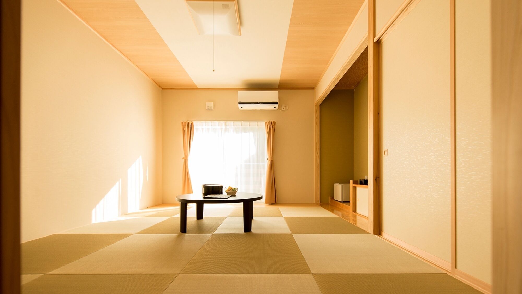 Ein Zimmer mit Tatami-Boden, einem kleinen Tisch mit einer Schale, einer weißen Klimaanlage und einer Schiebetür zu einem weiteren Raum.
